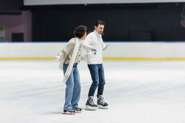 Casal multiétnico positivo se divertindo enquanto patinação no gelo na pista — Fotografia de Stock