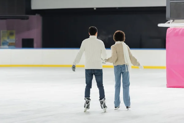 Back view of interracial couple ice skating together on rink — Stock Photo