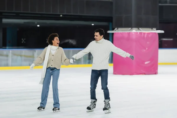 Excited african american woman ice skating with boyfriend on rink — Stock Photo