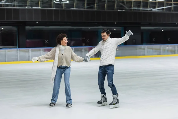 Positives multiethnisches Paar in Handschuhen Eislaufen und Spaß auf der Eisbahn — Stockfoto