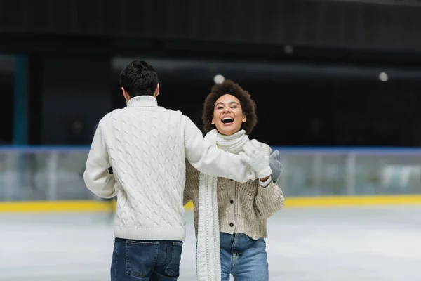 African american woman laughing while ice skating with boyfriend on ice rink — Stock Photo