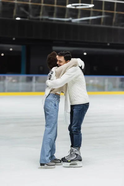 Homme souriant en pull embrassant la petite amie afro-américaine sur la patinoire — Photo de stock