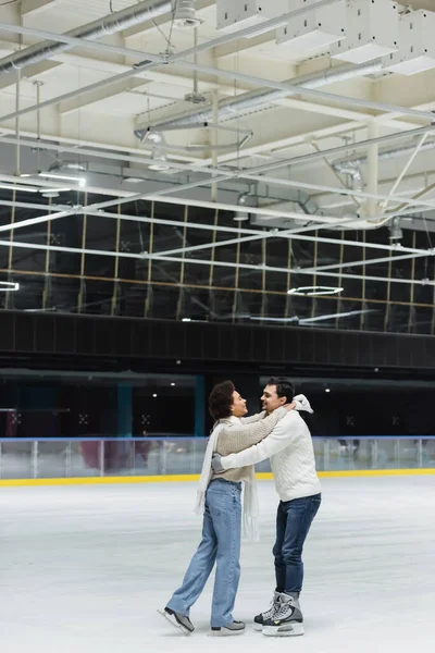 Vista lateral da mulher americana africana alegre abraçando namorado na pista de gelo — Fotografia de Stock