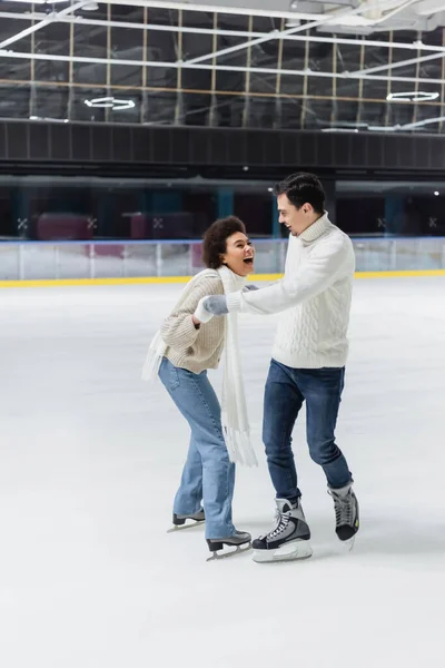 Excited african american woman holding hands of boyfriend while ice skating on rink — Stock Photo