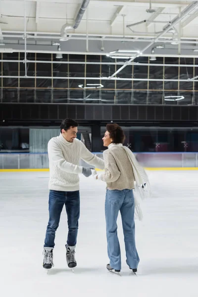 Positive multiethnic couple holding hands while skating on ice rink during date — Stock Photo
