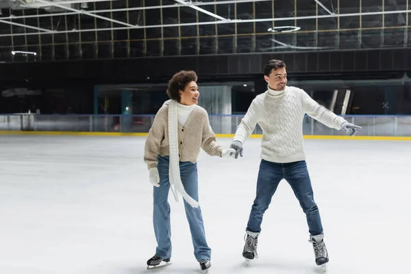 Young man pointing with finger and ice skating with african american girlfriend on rink — Stock Photo