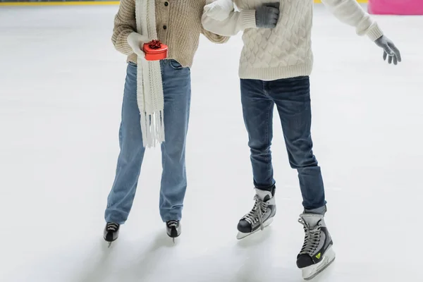 Cropped view of woman in gloves holding heart shaped gift near boyfriend on ice rink — Stock Photo