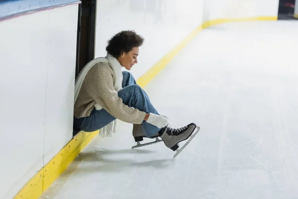 Side view of smiling african american woman wearing ice skates on rink — Stock Photo