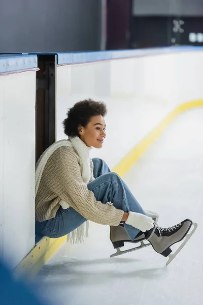 Positive Afroamerikanerin trägt Schlittschuhe und schaut auf Eisbahn weg — Stockfoto