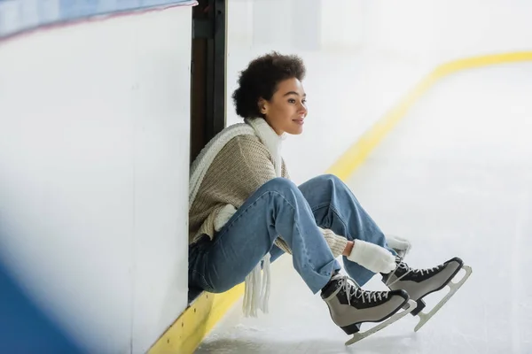 Happy african american woman wearing ice skates on blurred rink — Stock Photo