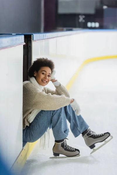 Sorridente donna africana americana in pattini di ghiaccio guardando la fotocamera sulla pista di pattinaggio — Foto stock