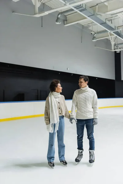Smiling multiethnic couple holding hands while spending time on ice rink — Stock Photo