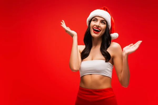 Sexy donna bruna in cima e cappello da Babbo Natale guardando isolato sul rosso — Foto stock