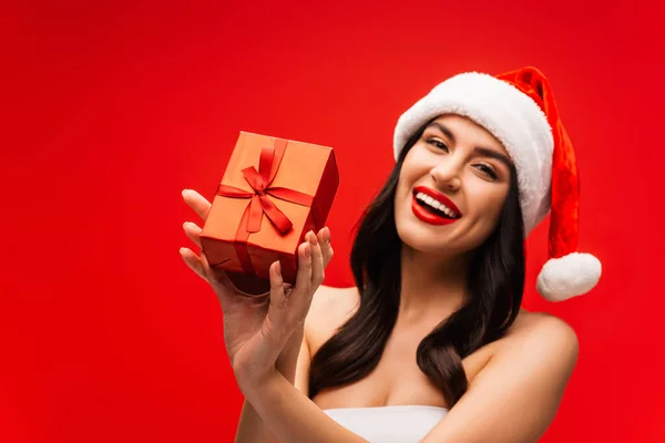 Fröhliche junge Frau mit Weihnachtsmütze und Geschenkbox auf Rot — Stockfoto