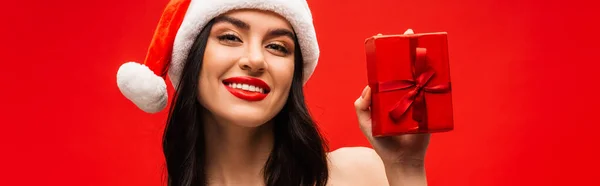 Ritratto di donna positiva in cappello da Babbo Natale con fiocco isolato sul rosso, stendardo — Foto stock