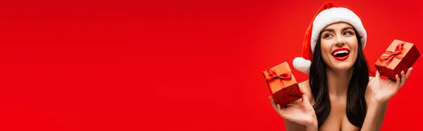 Fröhliche junge Frau in Weihnachtsmannmütze mit Geschenken auf rotem Grund mit Kopierraum, Banner — Stockfoto