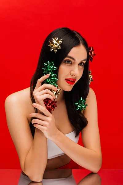 Bella donna bruna in alto che tiene archi regalo vicino allo specchio isolato sul rosso — Foto stock