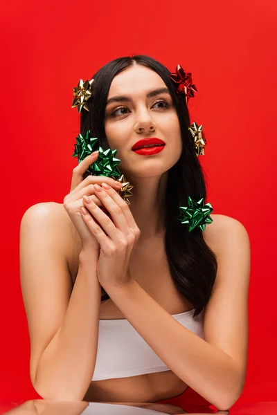 Portrait of young woman with naked shoulders holding gift bows near mirror isolated on red — Stock Photo