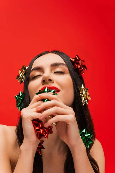 Молодая женщина с макияжем и подарочные банты на волосы изолированы на красный — стоковое фото