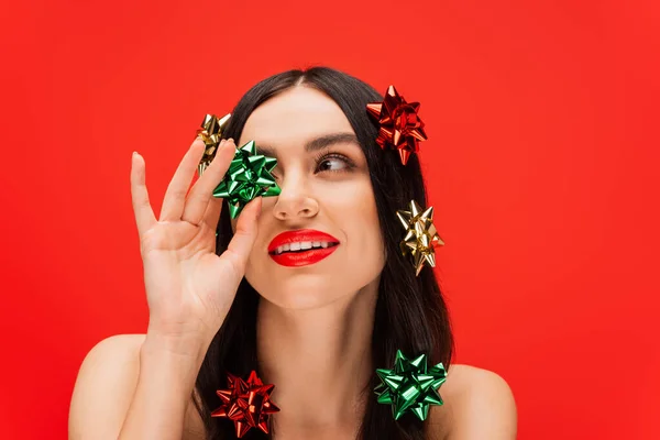 Mujer joven con maquillaje y brillantes lazos de regalo en el cabello aislado en rojo - foto de stock