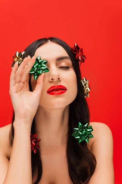 Young model with naked shoulders holding gift bow isolated on red — Stock Photo