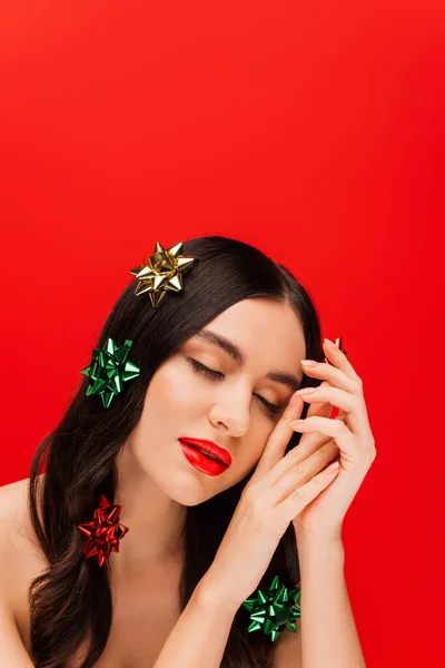 Femme avec visage et noeuds cadeaux sur les cheveux posant isolé sur rouge — Photo de stock