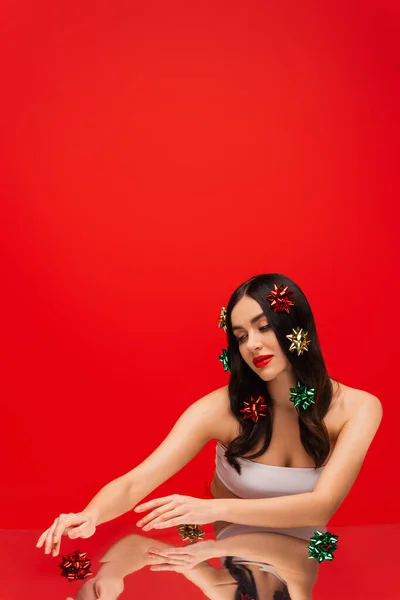 Giovane donna con il trucco toccante regalo archi sulla superficie riflettente isolato sul rosso — Foto stock