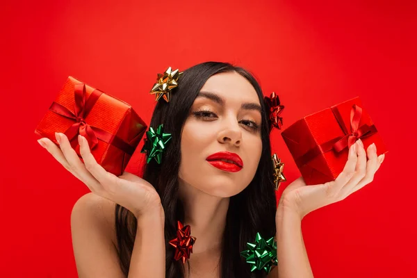 Portrait woman with makeup and gift bows on hair holding presents isolated on red — Stock Photo