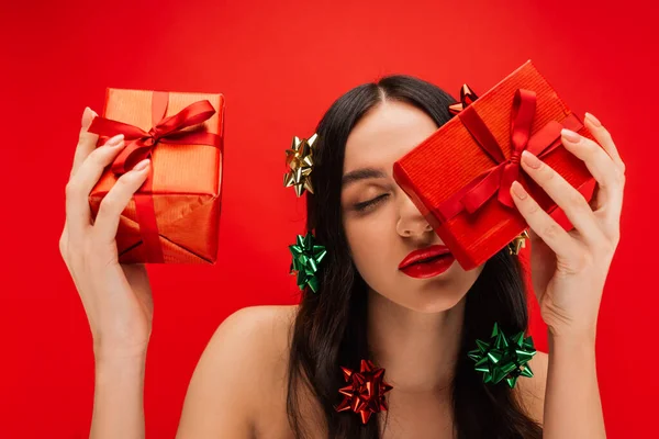 Woman with gift bows on hair holding presents isolated on red — Stock Photo