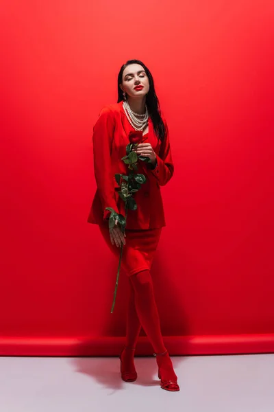 Toute la longueur de la jeune femme élégante tenant rose sur fond rouge — Photo de stock