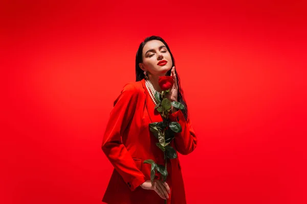 Pretty brunette woman in jacket holding rose isolated on red — Stock Photo