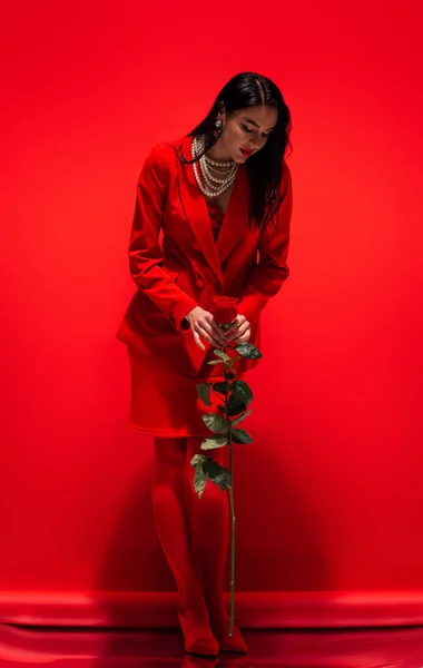 Элегантная женщина в жемчужном ожерелье держа розу на красном фоне — стоковое фото