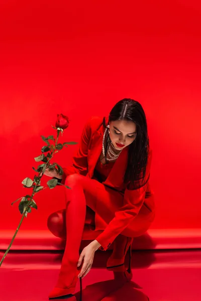 Brünette Frau in High Heels und Rock mit Rose auf rotem Hintergrund — Stockfoto