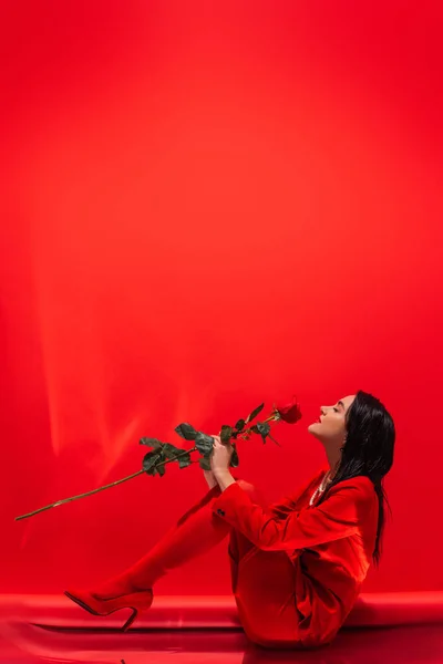 Side view of elegant woman in heels holding rose on red background with copy space — Stock Photo