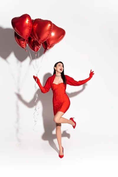 Захоплена жінка в одязі і підборах тримає кульки у формі червоного серця на білому тлі з тіні — стокове фото