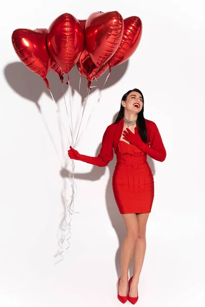 Stylish woman in red clothes laughing and holding heart shaped balloons on white background with shadow — Stock Photo