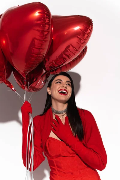 Mulher morena excitada em casaco vermelho segurando balões em forma de coração no fundo branco com sombra — Fotografia de Stock