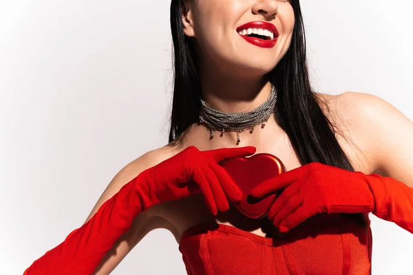 Vista cortada de mulher alegre em luvas vermelhas segurando presente em forma de coração isolado no branco — Fotografia de Stock