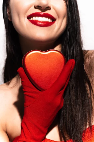 Vista recortada de mujer sonriente con labios rojos sosteniendo presente en forma de corazón aislado en blanco - foto de stock