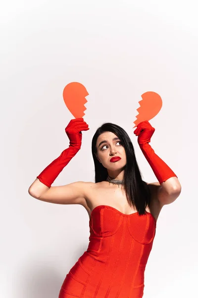 Femme pensive en robe rouge tenant coeur en papier cassé sur gris — Photo de stock
