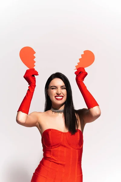 Веселая и стильная женщина с красными губами, держащая разбитое бумажное сердце на сером — стоковое фото