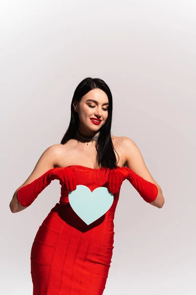 Стильная женщина в красном платье и перчатках с бумажным сердцем, изолированным на сером — стоковое фото
