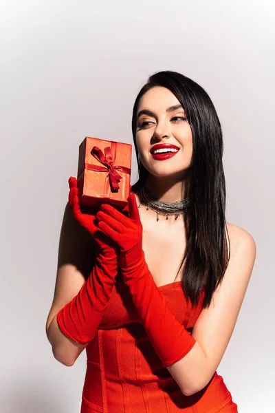 Stilvolle brünette Frau in roten Handschuhen hält Geschenkbox auf grauem Hintergrund — Stockfoto