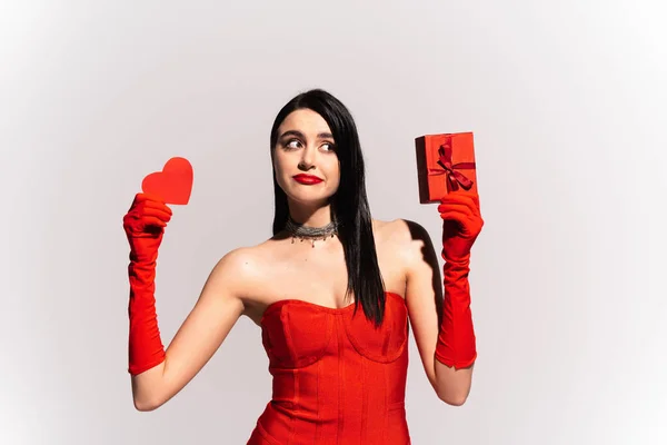 Frau in rotem Kleid hält Papierherz und Geschenk isoliert auf grau — Stockfoto