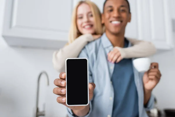 Selective focus of smartphone with blank screen in hand of blurred african american man near smiling woman — Stock Photo