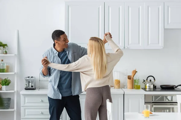 Sourire homme afro-américain dansant avec jeune copine blonde dans la cuisine — Photo de stock