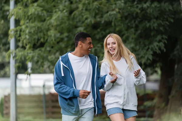 Excited blonde woman gesturing while talking to african american boyfriend in park — Stock Photo