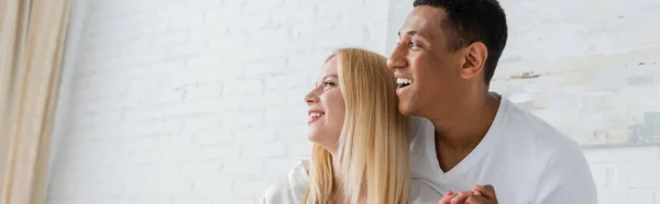 Femme blonde heureuse et homme afro-américain regardant loin à la maison, bannière — Photo de stock