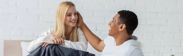 African american man touching hair of blonde girlfriend in bedroom, banner — Stock Photo