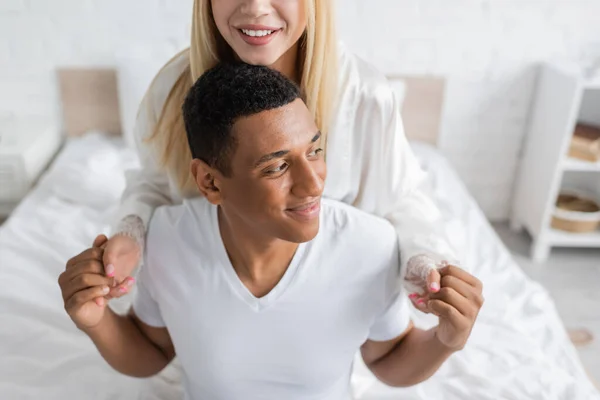 Lächelnder afrikanisch-amerikanischer Mann hält Händchen mit glücklicher Freundin, während er im Schlafzimmer wegschaut — Stockfoto